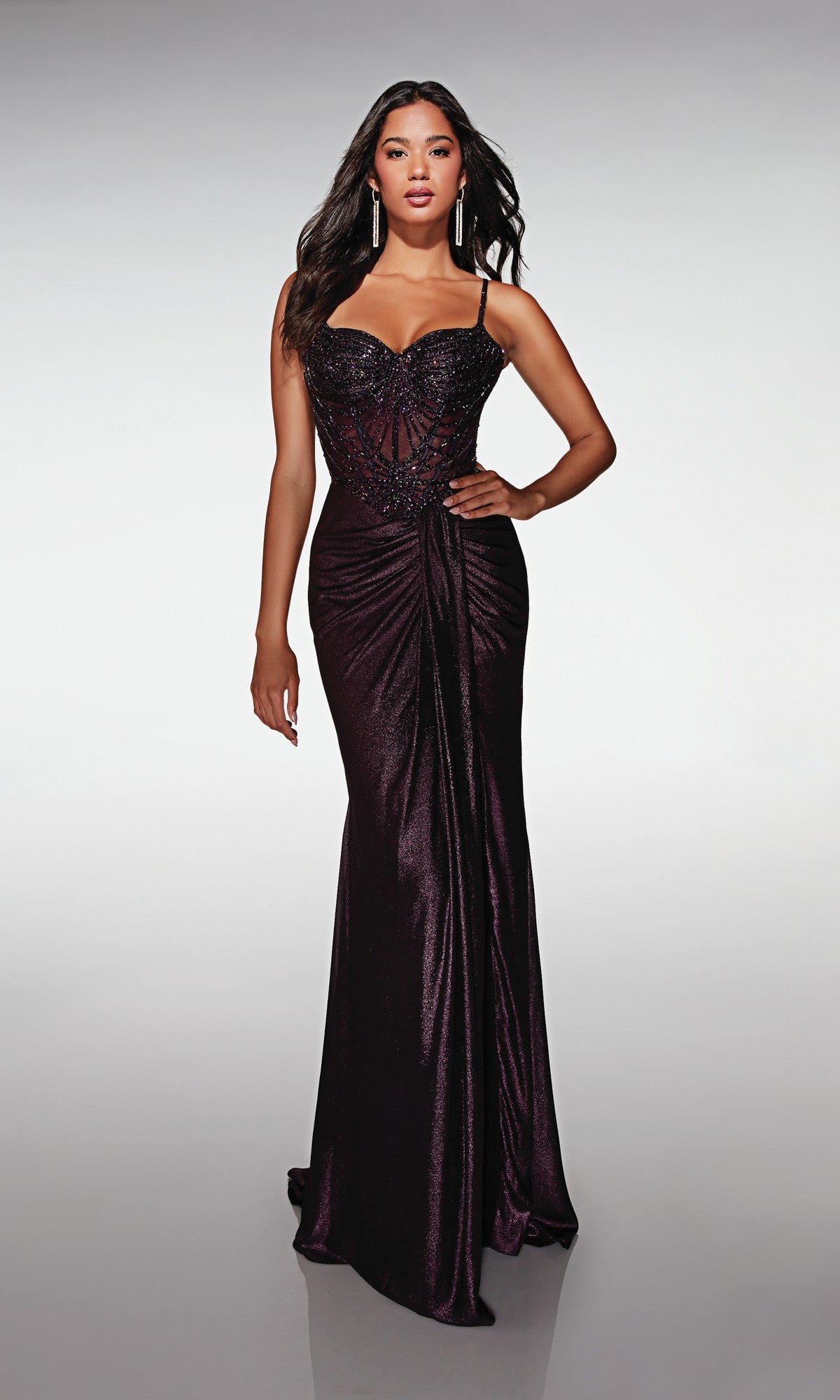 A woman models the Alyce 62143 long formal dress, featuring thin straps, a beaded and embellished corset bodice, and a draped front. She stands against a plain background.